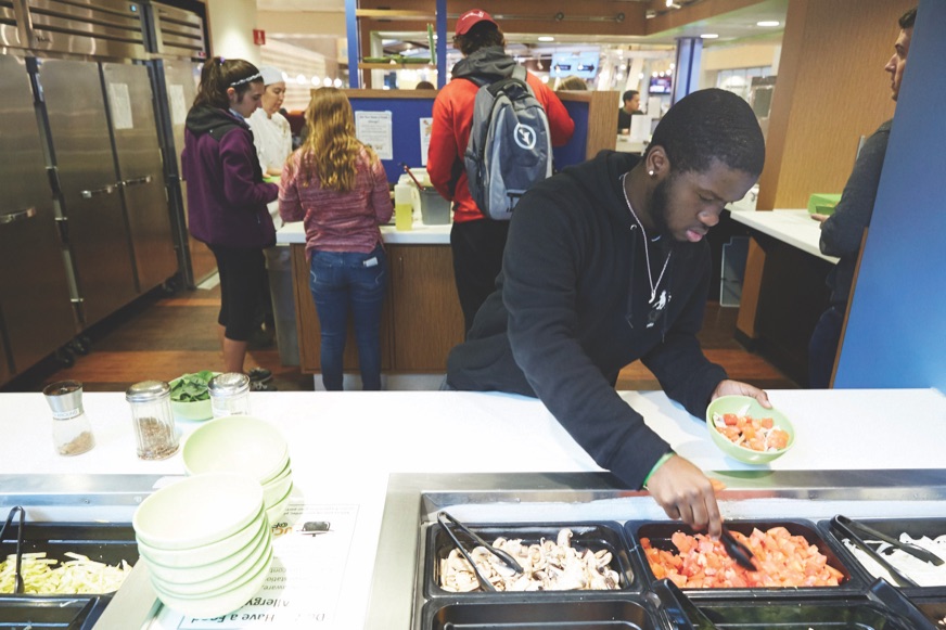 A student serving himself from a hot food counter in a campus dining hall.