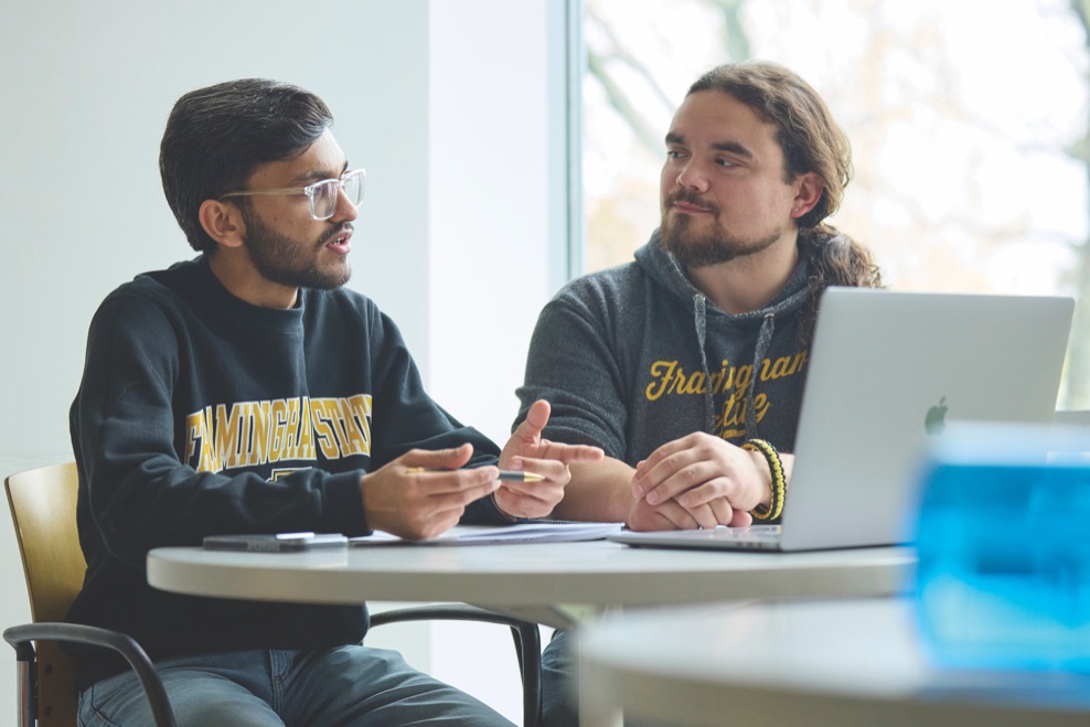 Shubham Valand seated at a table in a campus building, wearing a Framingham State sweatshirt.