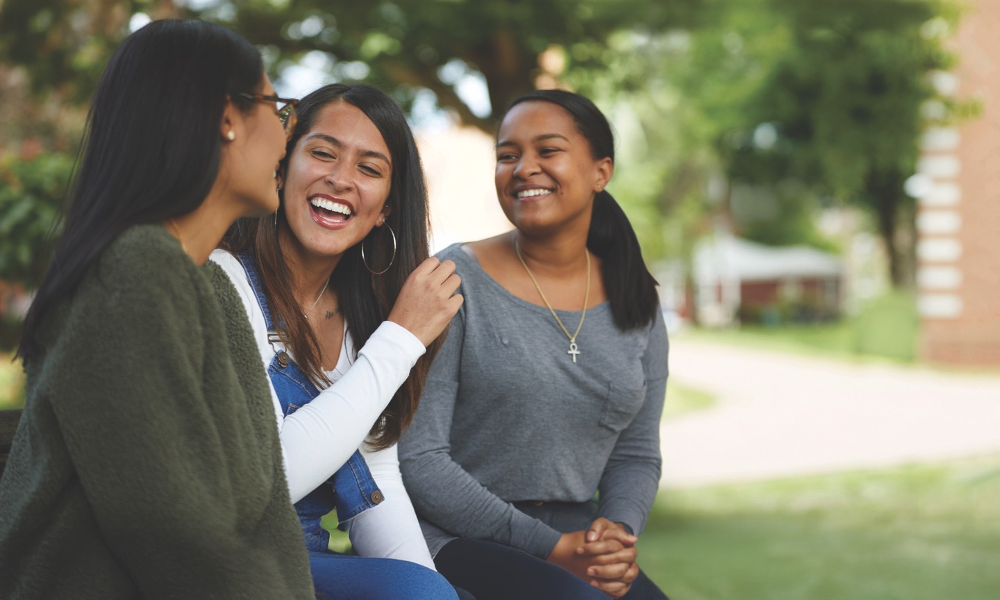 Three students laughing together outdoors on campus.
