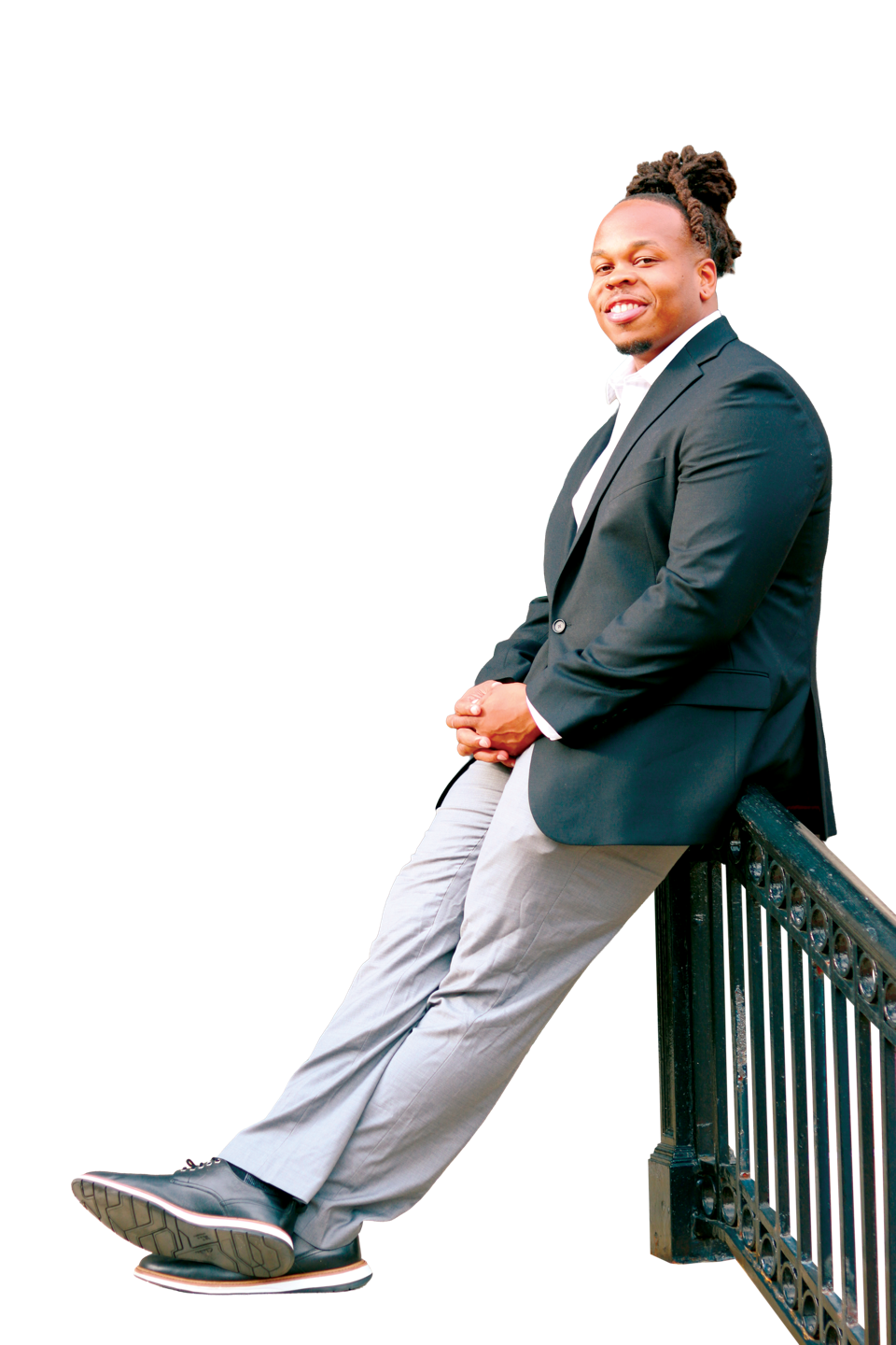 Deron Hines, Class of 2018, sociology graduate and member of the Chelsea City Council, leaning against a wrought-iron railing in a suit.