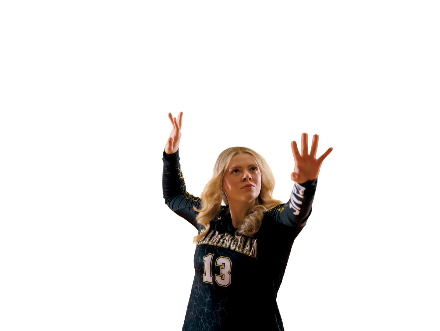 Natalie Reynolds in a black Framingham State jersey, number 13, reaching up with both hands having just set a volleyball.